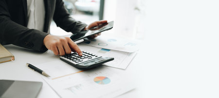 Young asian male work with financial papers at home count on calculator before paying taxes receipts...
