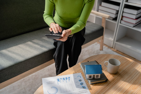 woman sitting on cozy sofa and planning and calculate expense and mortgage with calculator and home on desk, insurance and budget of residential, loan and residence, business and property conceptの写真素材