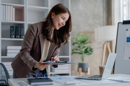 Portrait of a thoughtful Asian businesswoman looking at financial statements and making marketing plans using a computer on her desk.の写真素材
