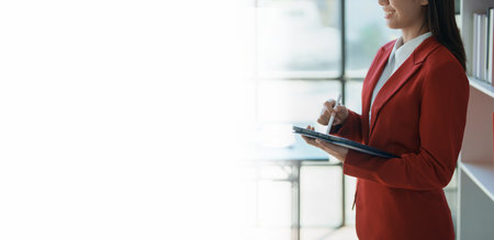 Young businesswoman professional business woman executive, female company or manager holding digital tablet using pad technology device working standing in modern corporate office. copy space conceptの写真素材