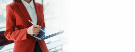 Young businesswoman professional business woman executive, female company or manager holding digital tablet using pad technology device working standing in modern corporate office. copy space conceptの写真素材