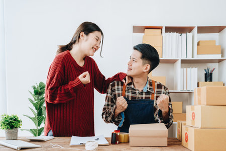 A young Asian couple shows delight and smiles on their faces when they see the sales volume and customer orders exceed expectations. sme or small business family concepts.の写真素材