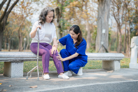 Patient care, female care, young Asian women are taking care of the elderly, providing crutches and walking for patients, and exercising their legs and knees in the park parksの写真素材