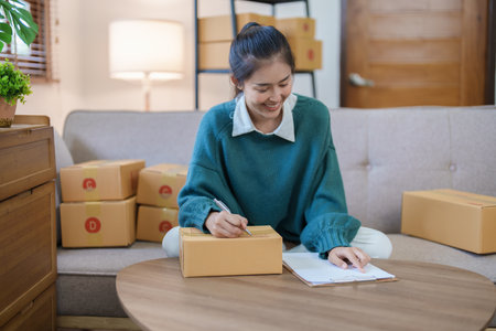 Starting small business entrepreneur of independent Asian female online seller packing products to...