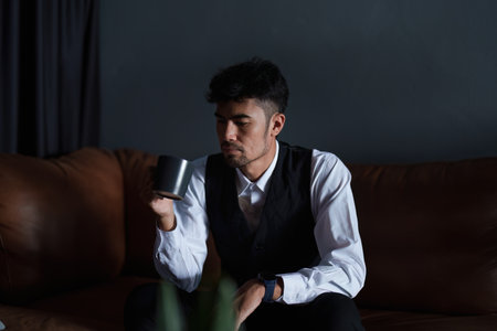 Portrait of a good looking and discreet Asian man sitting on the sofa drinking coffee.の写真素材