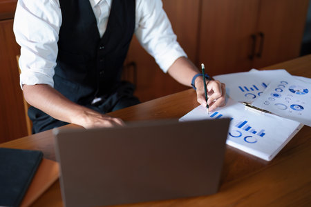 A portrait of a good-looking and discreet Asian man sitting at his desk making a thoughtful face while reading budget papers and using a computer.の写真素材