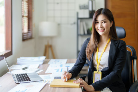 Portrait of a woman business owner showing a happy smiling face as he has successfully invested her business using computers and financial budget documents at work.の写真素材