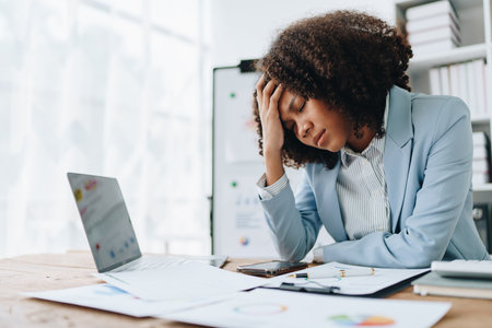 Burnout American African business woman in stress works with many paperwork document, migraine attack, Freelance, work at office.の写真素材