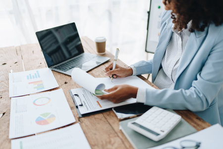 Beautiful young African american businesswoman using laptop computer and paperworks with planning working on financial document, tax, exchange, accounting and Financial advisor.の写真素材