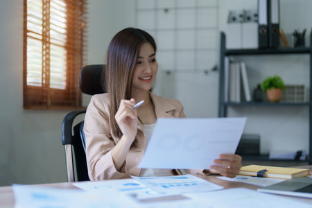 Young asian businesswoman manager, lawyer or company employee holding accounting bookkeeping documents checking financial data or marketing report working in office with laptop. Paperwork management.の写真素材