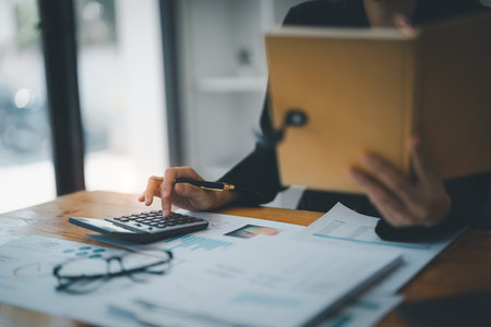 Young asian female work with financial papers at home count on calculator before paying taxes receipts online, planning budget glad to find chance for economy saving money, audit concepts.の写真素材