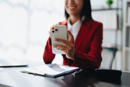 Portrait of beautiful young businesswoman standing smiling and using smartphone.の写真素材