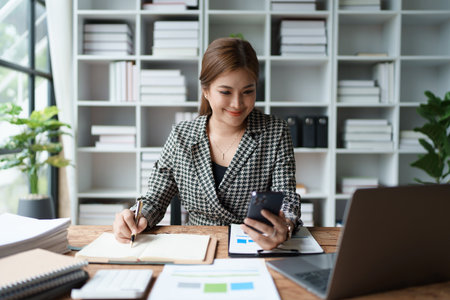 Consultant, advisor, Asian business woman working on the computer and using smartphone mobile talking work financial and marketing business planning company profits, marketing planning budgetの写真素材