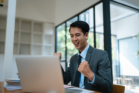 Portrait of an Asian male business owner standing with a computer showing happiness after a successful investment.の写真素材