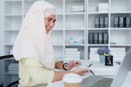 Muslim women use calculators, computers, and laptops to check their accounts at workの写真素材
