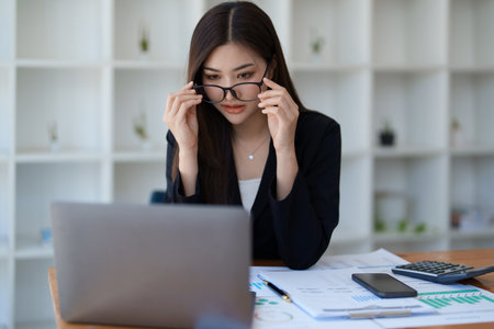 Young asian businesswoman manager, lawyer or company employee holding accounting bookkeeping documents checking financial data or marketing report working in office with laptop. Paperwork management.の写真素材