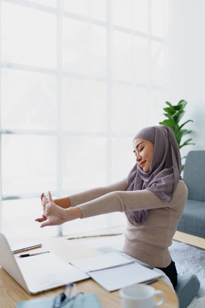 Muslim undergraduate students relax their muscles after taking online e-learning via computer systemの写真素材