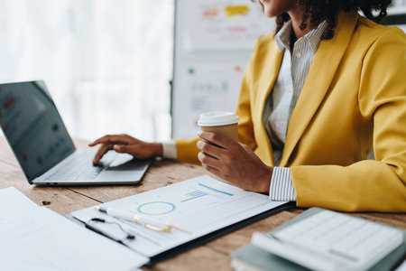 Beautiful young African american businesswoman using laptop computer and paperworks with planning working on financial document, tax, exchange, accounting and Financial advisor.の写真素材