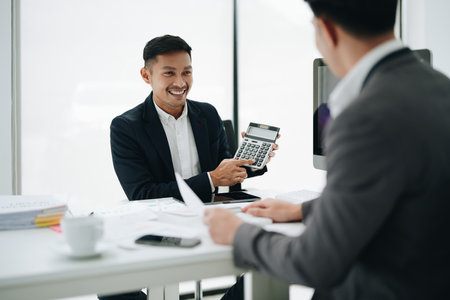 Two business people meeting to talking or discuss marketing work in workplace using paperwork, calculator, computer to work.の写真素材