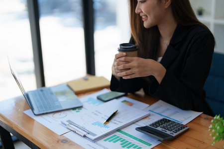 Portrait of a woman business owner showing a happy smiling face as he has successfully invested her business using computers and financial budget documents at work.の写真素材