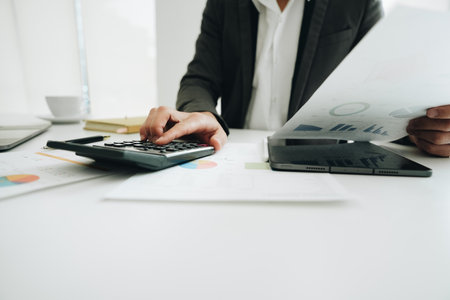 businessman or accountant working on calculator and laptop computer to calculate business data during using accountancy document at officeの写真素材