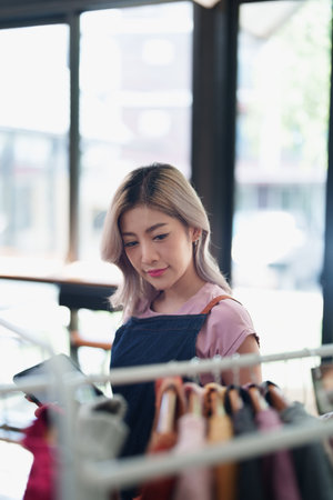 Portrait Of Asian Female Owner Of Fashion Store Checking Stock In Clothing Store With using notebook successful happy smile at small business, sme or ecommerce concepts.の写真素材
