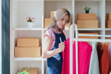Portrait Of Asian Female Owner Of Fashion Store Checking Stock In Clothing Store With using notebook successful happy smile at small business, sme or ecommerce concepts.の写真素材