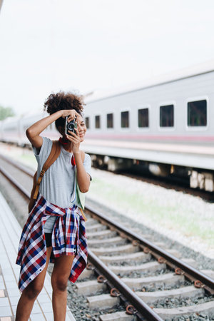 Asian teenage girl african american traveling using a camera take a photo to capture memories while waiting for a train at the stationの写真素材