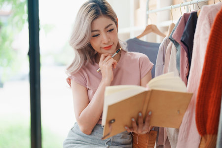 Starting small business entrepreneur of independent young Asian woman online seller is using computer and taking orders to pack products for delivery to customers. SME delivery concept.の写真素材