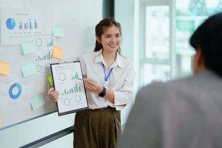 portrait of young asian business team presents business profits to colleagues at meeting, explaining business turn over on flipchart to coworkers in office with using tabletの写真素材