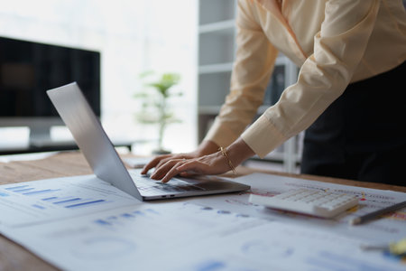 woman meticulously plans a finance audit, using a computer and calculator to review budget documents and ensure accuracy.の写真素材