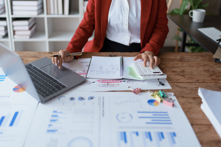 woman meticulously plans a finance audit, using a computer and calculator to review budget documents and ensure accuracy.の写真素材