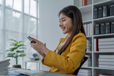 Young professional woman smiling while using smartphone in modern office environment with natural light.の写真素材