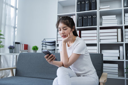 Woman is sitting on a couch using a smartphone while enjoying a relaxing moment at home.の写真素材