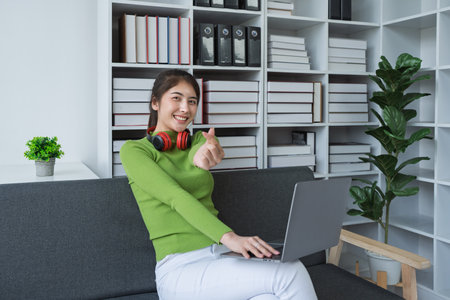 Woman with make mini heart symbol, wearing headphones using her computer at home.の写真素材