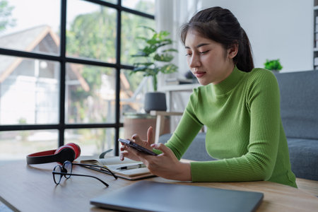 Woman at a table using smartphone and laptop while engaging in social media and online shopping activities at home.の写真素材