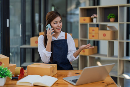 Young woman engaged in online business in a smartphone conversation while managing delivery products customer in a modern office environment.の写真素材