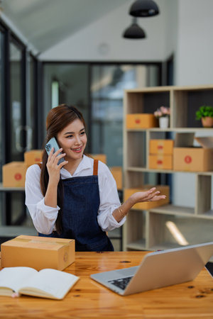 Young woman engaged in online business in a phone conversation while managing deliveries products customer in a modern office environment.の写真素材