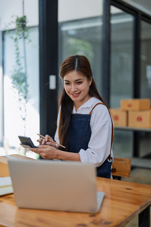 Young woman engaged in online business working analyze data customer in computer laptop with using calculator to calculate profit with Selling products of This monthの写真素材