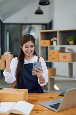Excited young woman celebrating success while using smartphone to see data delivery products customer profit Selling products of This month.の写真素材