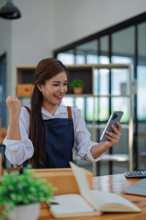 Excited young woman celebrating success while using smartphone to see data delivery products customer profit.の写真素材