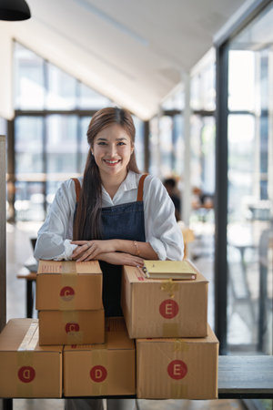 Young woman engaged in online business working with using notebook, preparing package for shipping and taking notes customer address at box.の写真素材