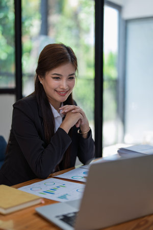 Confident business woman smiling Show successful gestures at her desk with market charts and documents in office.の写真素材
