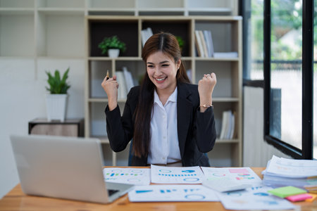 Confident business woman smiling Show successful gestures at her desk with market charts and documents in office.の写真素材