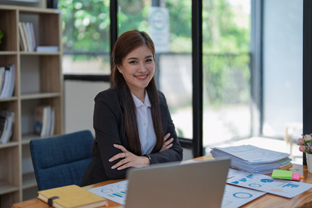 Confident business woman smiling Show successful gestures at her desk with market charts and documents in office.の写真素材