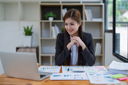 Confident business woman smiling Show successful gestures at her desk with market charts and documents in office.の写真素材