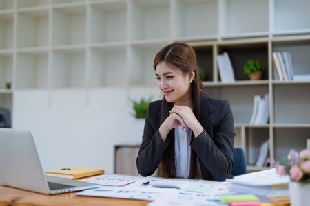 Confident business woman smiling Show successful gestures at her desk with market charts and documents in office.の写真素材