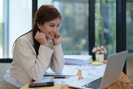 Confident business woman smiling Show successful gestures at her desk with market charts and documents in office.の写真素材
