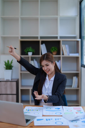Confident business woman smiling Show successful gestures at her desk with market charts and documents in office.の写真素材