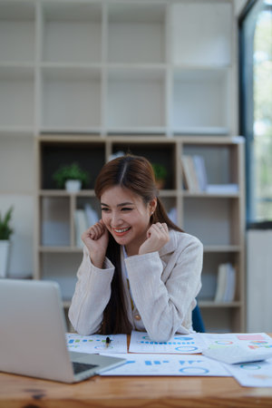 Confident business woman smiling Show successful gestures at her desk with market charts and documents in office.の写真素材